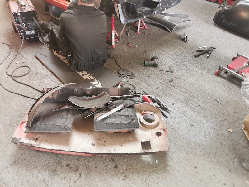 person sitting on the floor welding the Fiat 500 part of the fiat on the floor, restoration in progress
